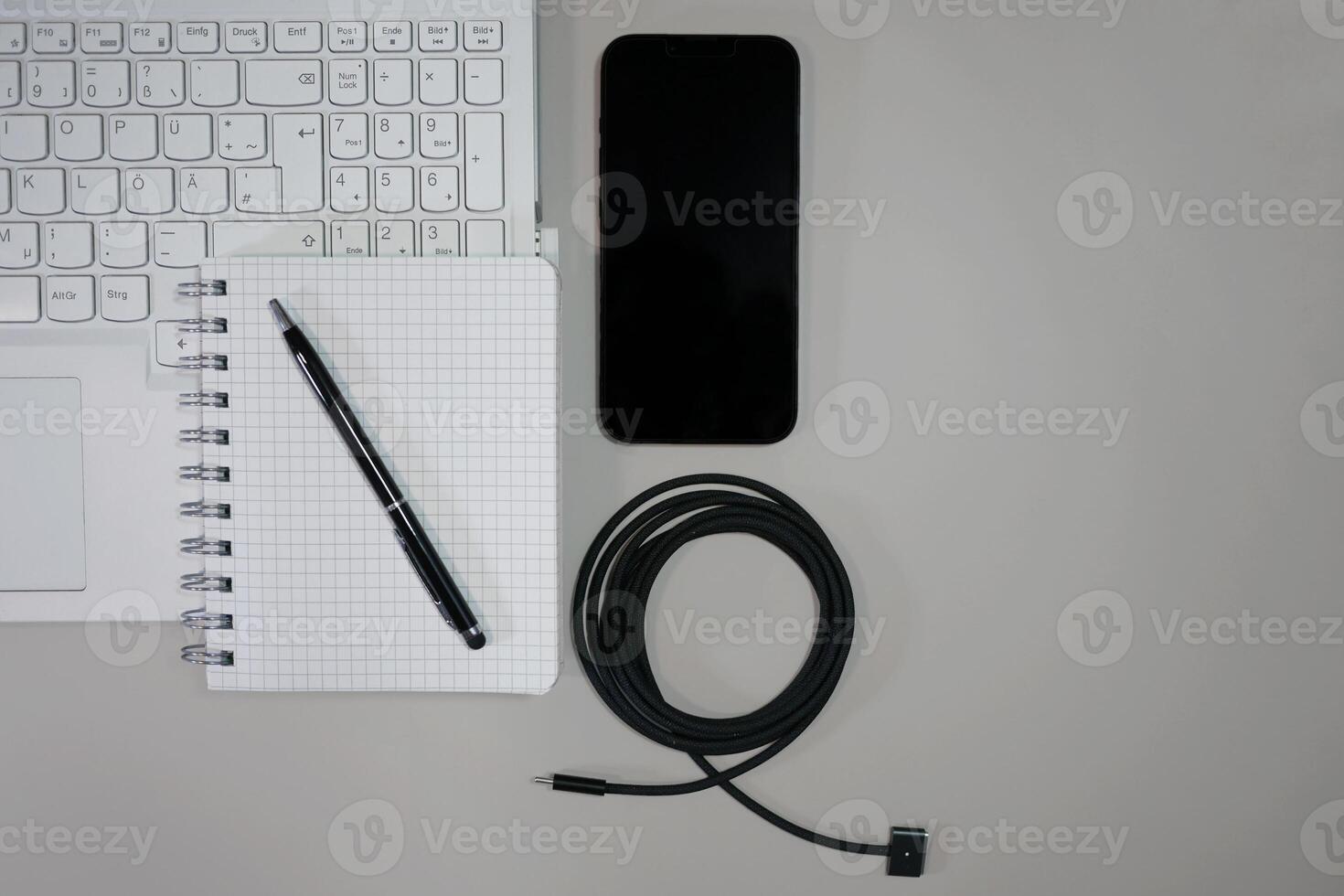 Flatlay on white background top view with copy space. Computer laptop keyboard, notebook, smartphone and cable. The concept of business, study or IT photo