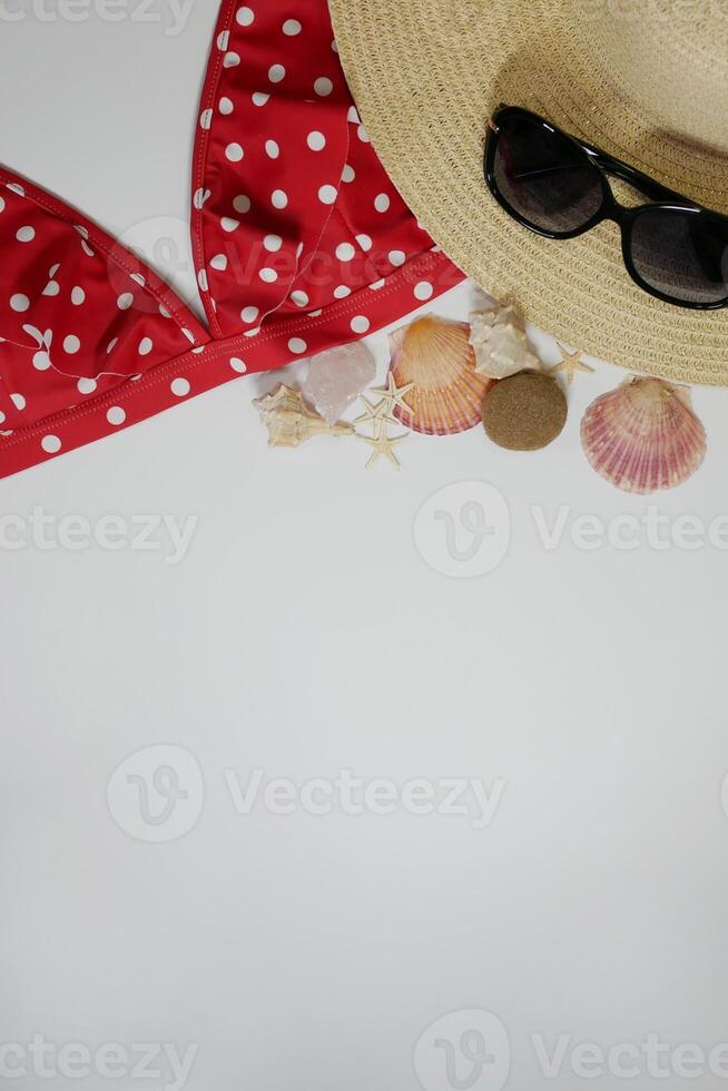 Summer travel vacation mood layout lifestyle spa wellness concept with beach accessories and copy space. Top view flat lay background, including straw hat, sunglasses, red swimsuit, seashells, pebbles photo