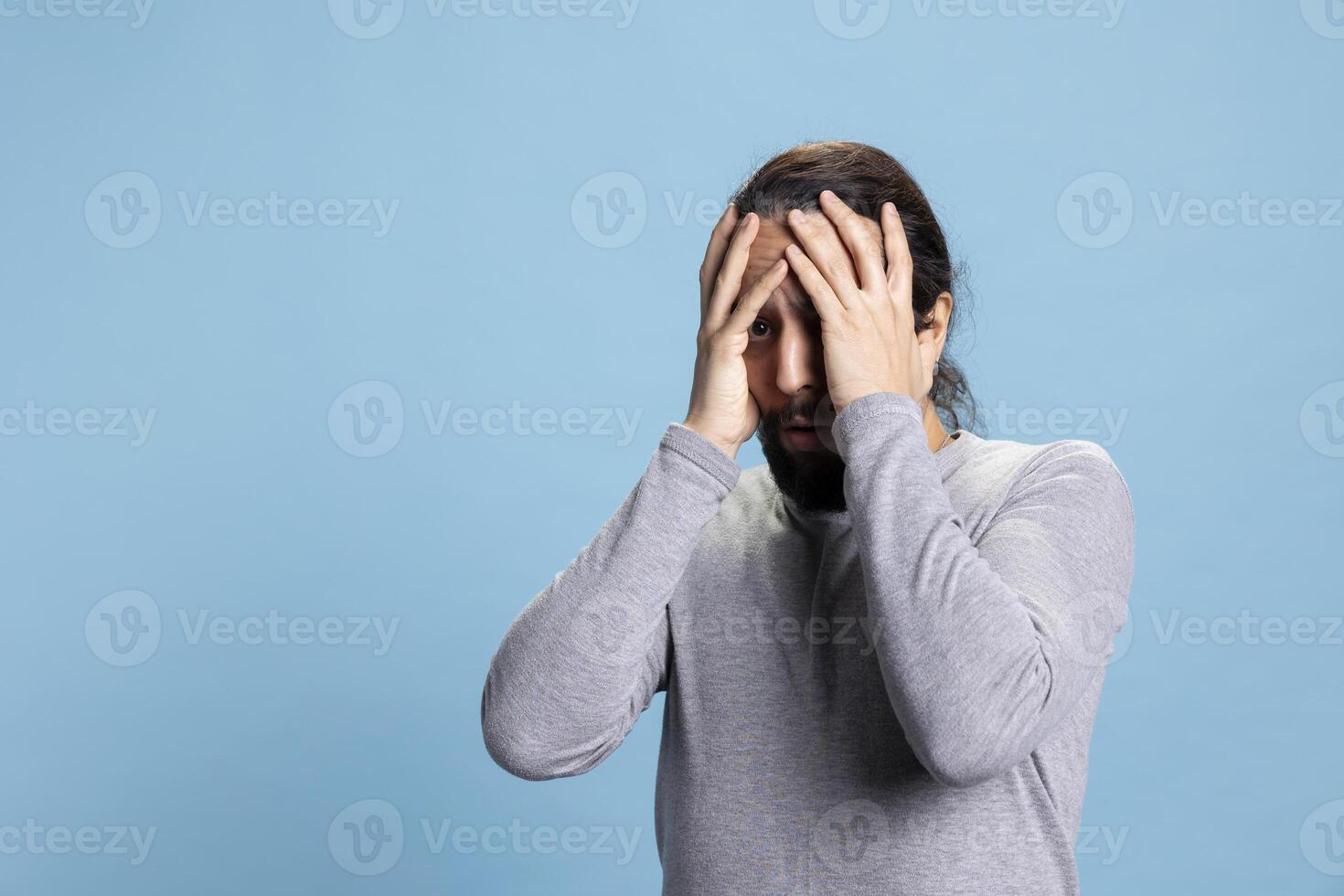 Horrified young guy in shock getting really scared and worried about something, being distraught and fearful against blue background. Afraid terrified man being frightened, horror reaction. photo
