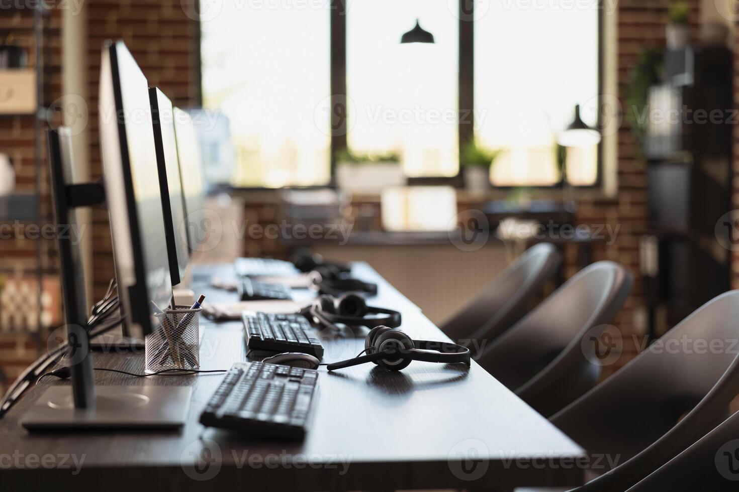 Empty workspace, with no person present, highlighting a modern business setting with desktop monitors. Multiple computers are neatly organized on desks in vacant brick wall office. photo