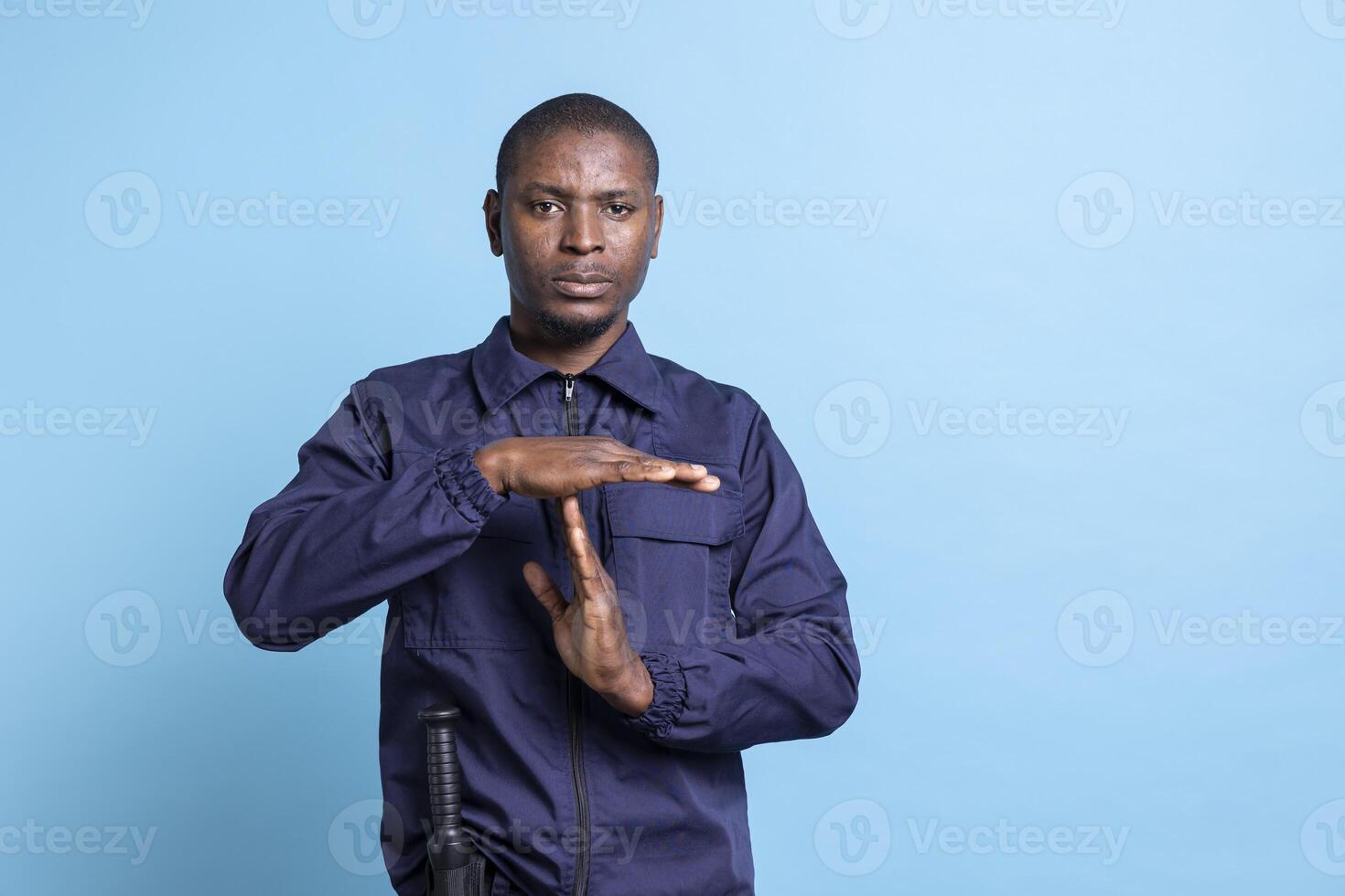 African american guard asking for a break with a timeout symbol in studio, feeling overworked with burnout on duty. Man in agent uniform presenting a pause gesture for relaxation. photo