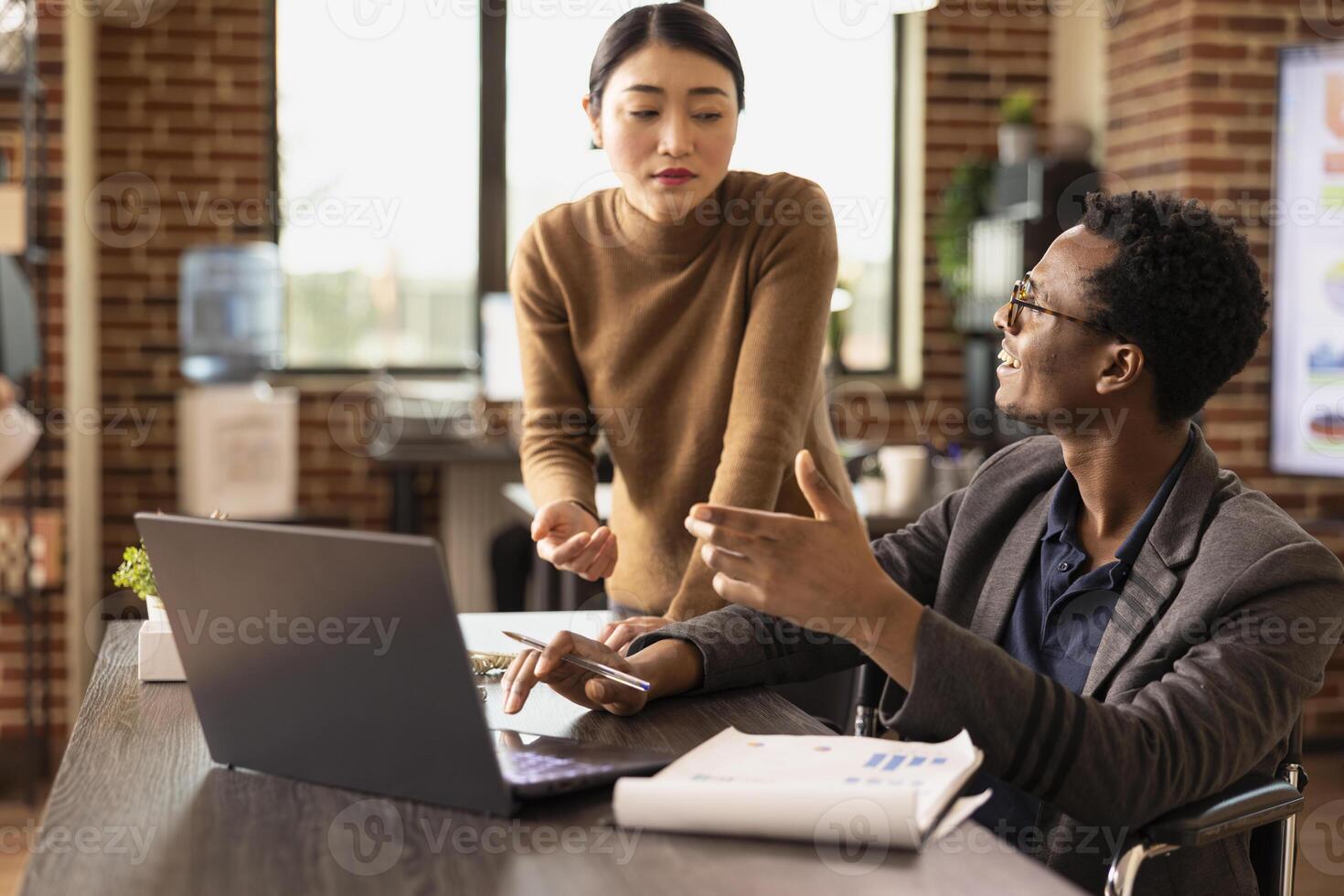 Male business analyst pointing at laptop and explaining strategy improvements to attentive coworker. Diverse colleagues checking financial reports, ensuring accuracy in business performance metrics. photo