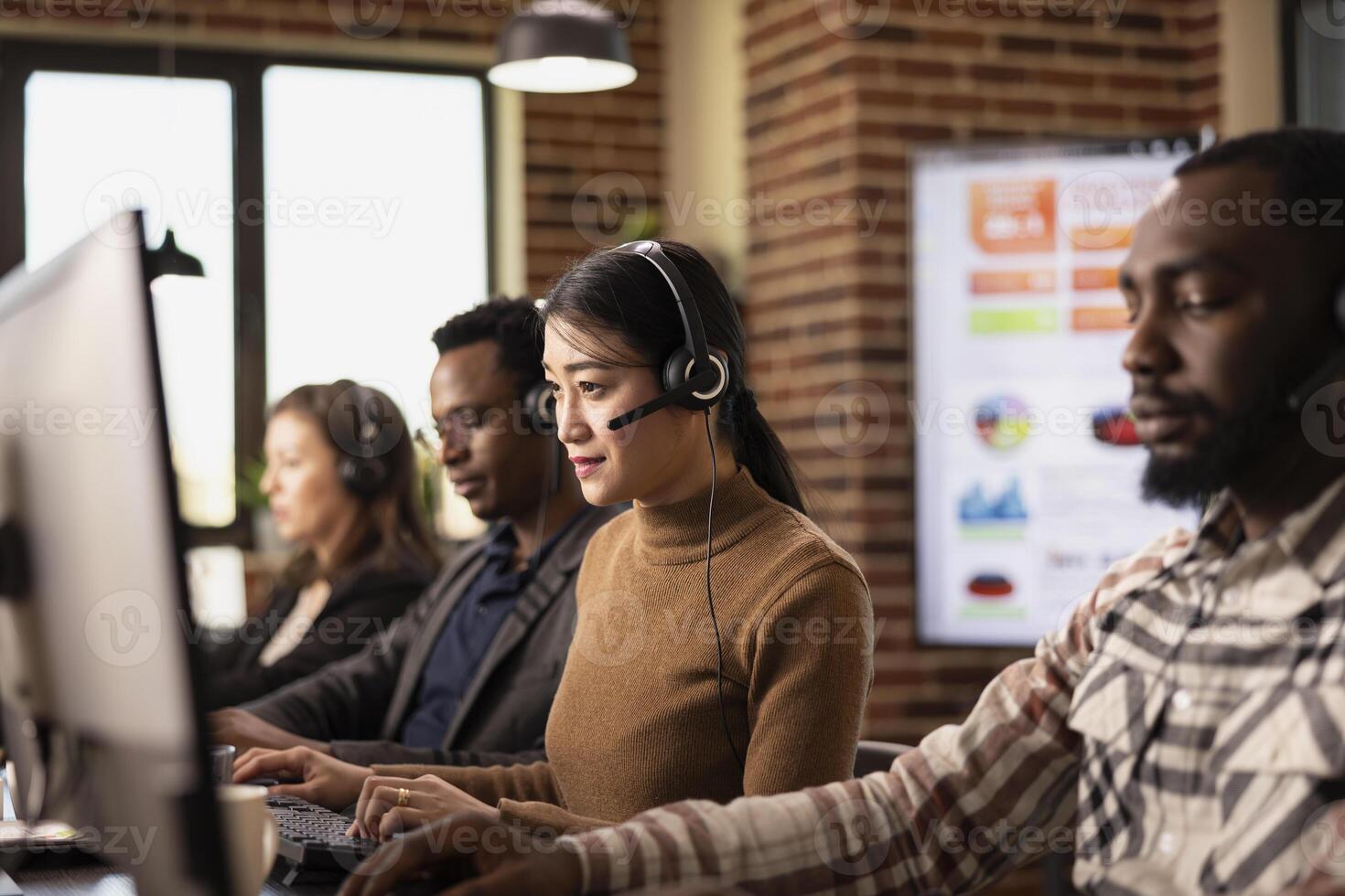 Multiethnic call center agents sit at their workstations, handling business inquiries and communicating with remote customers. Coffee, computers, and headsets set the office scene. photo