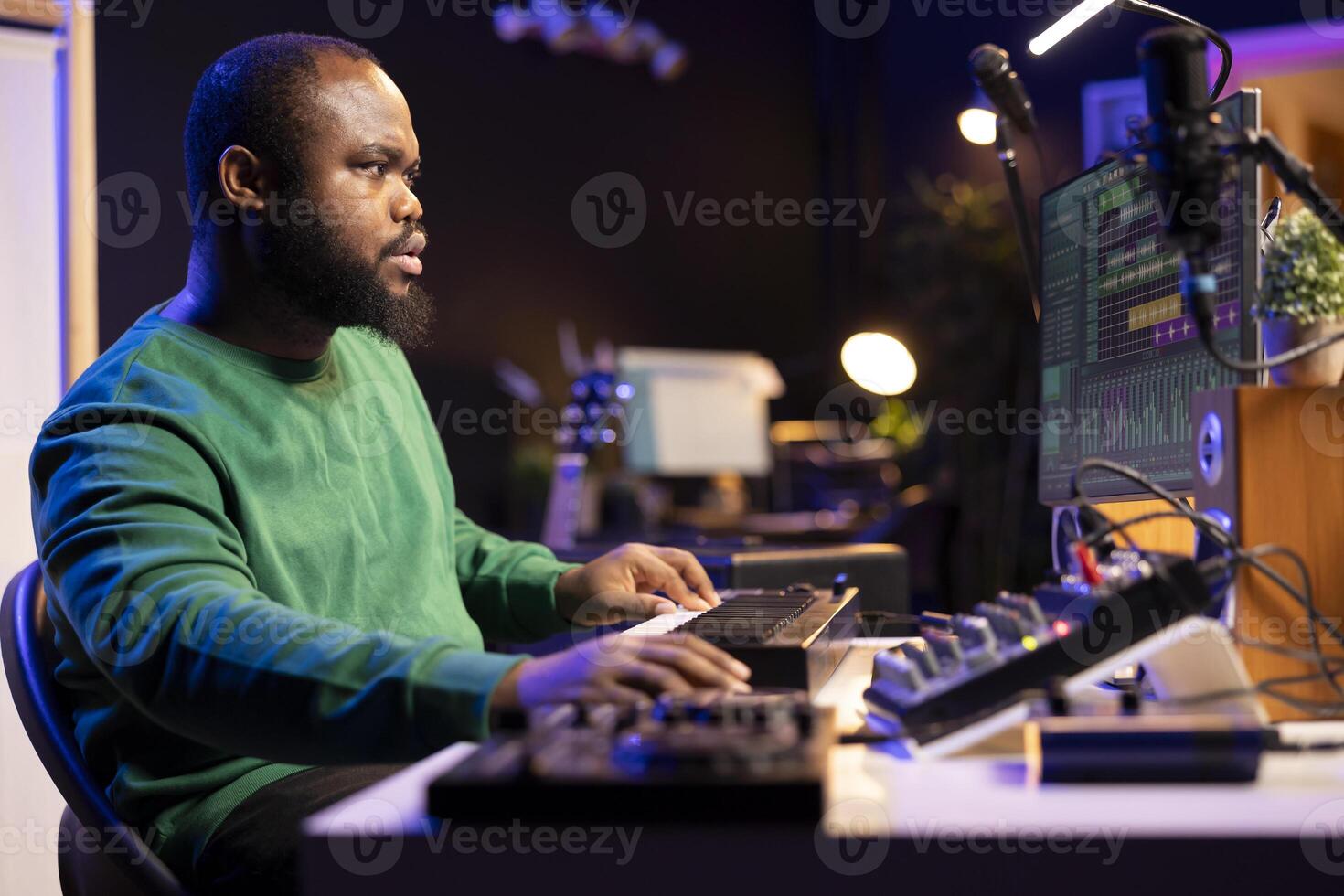 Skilled music producer creating new songs on midi controller synthesizer, working with mixing console and professional software on pc. Male artist using piano and mastering acoustical tunes. photo