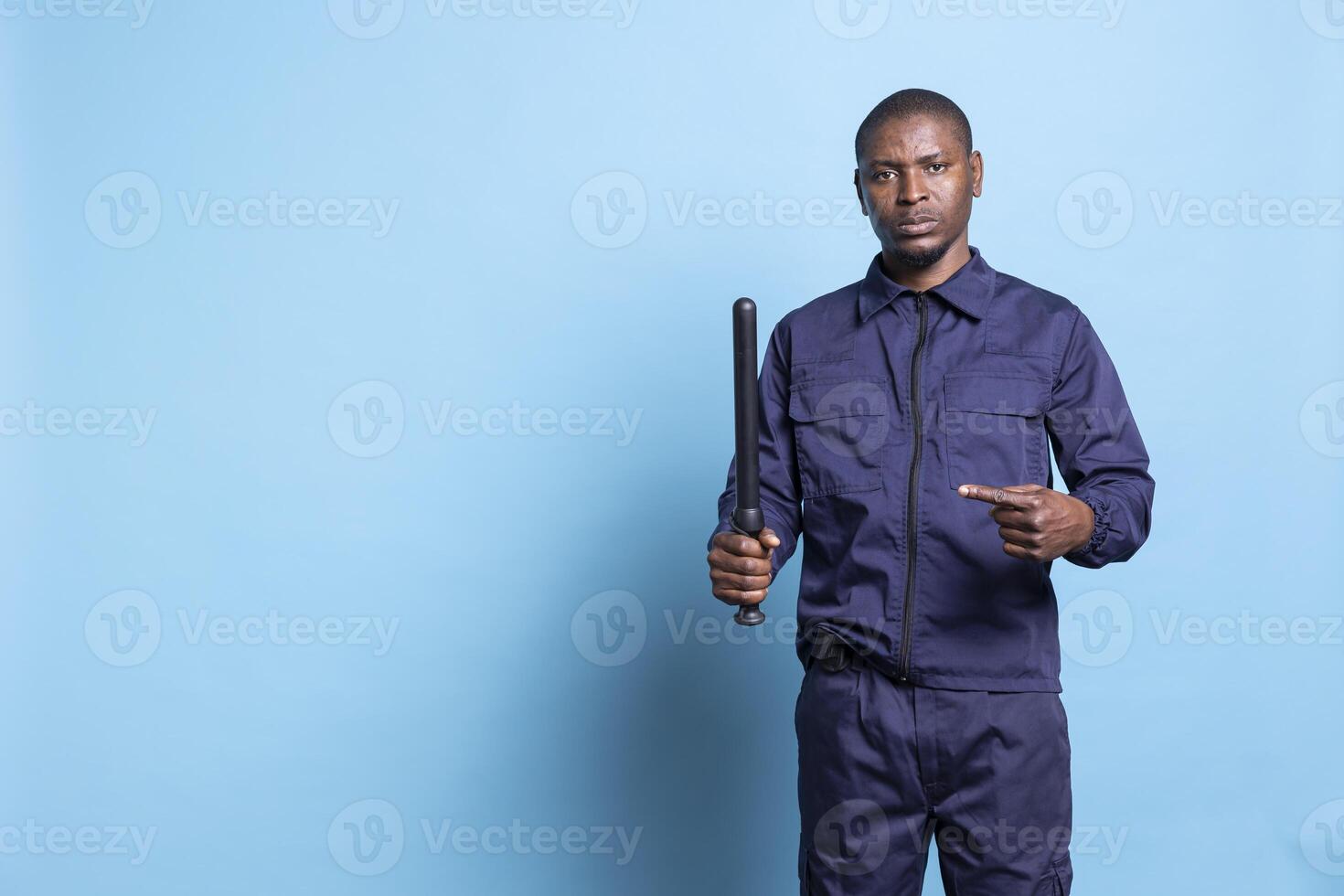 Trained security personnel pointing at his police baton in studio, presenting his weapon to use in case of emergency. African american armed guard is on patrol and protection duty. photo