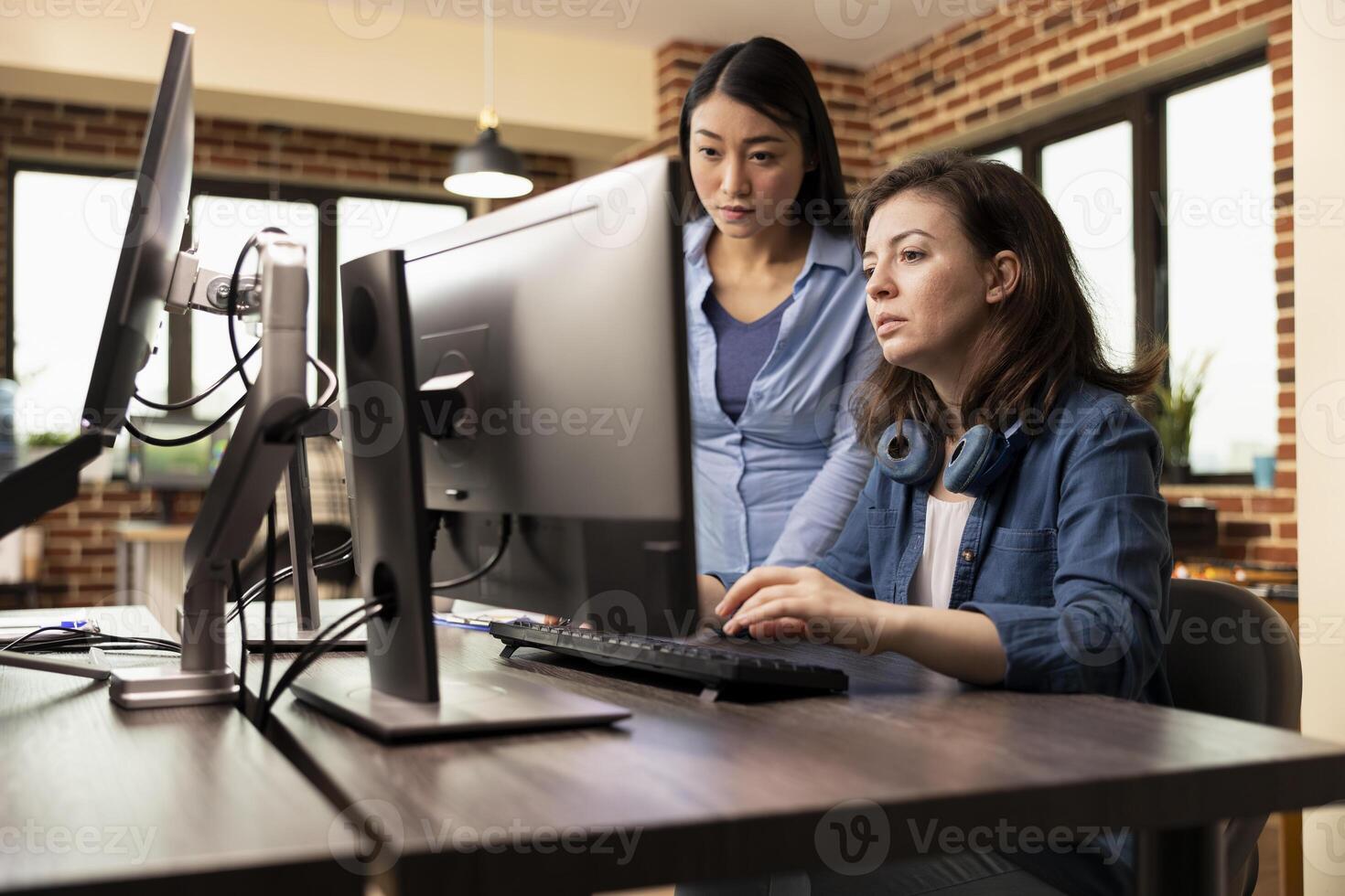 Creative agency female professionals collaborate in production department, brainstorming innovative ideas. Asian developer and caucasian colleague looking at computer screen, reviewing their designs. photo