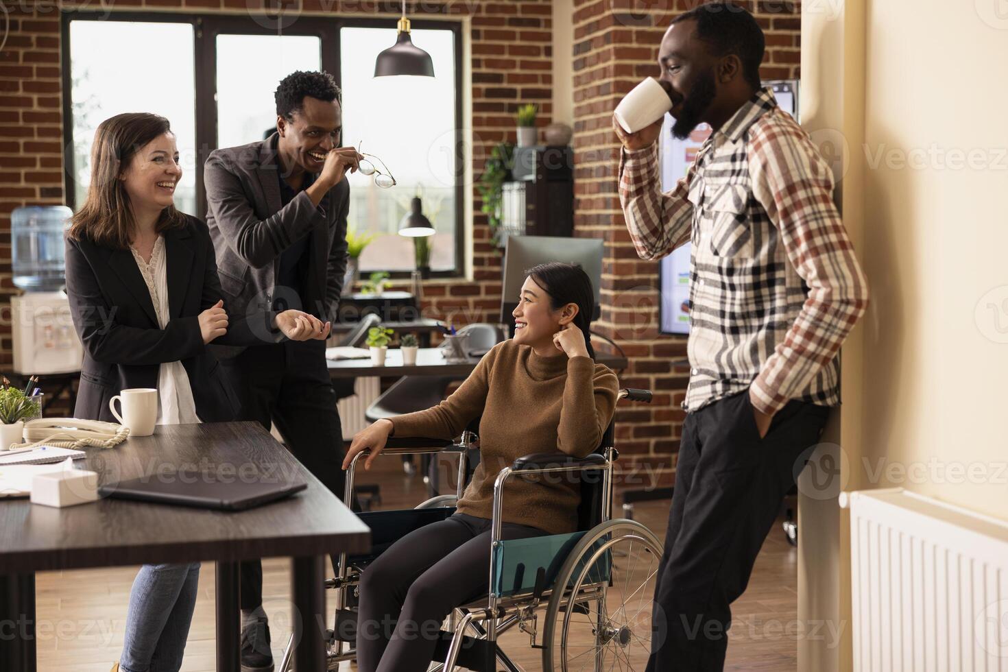 Colleagues enjoying casual office chatter, bonding over shared experiences in modern startup environment. Laughter fills the modern workspace as multiethnic employees take a break at the office desk. photo