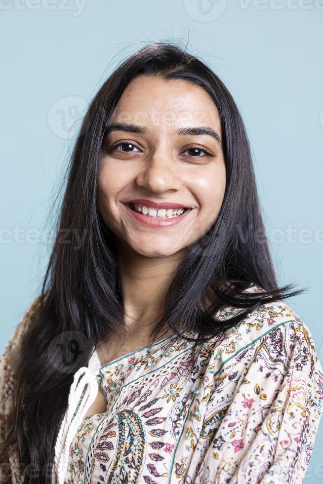 Portrait of smiling indian person posing in front of the camera, being happy and confident in herself. Upbeat friendly woman with long hair standing against blue background, freshness. photo