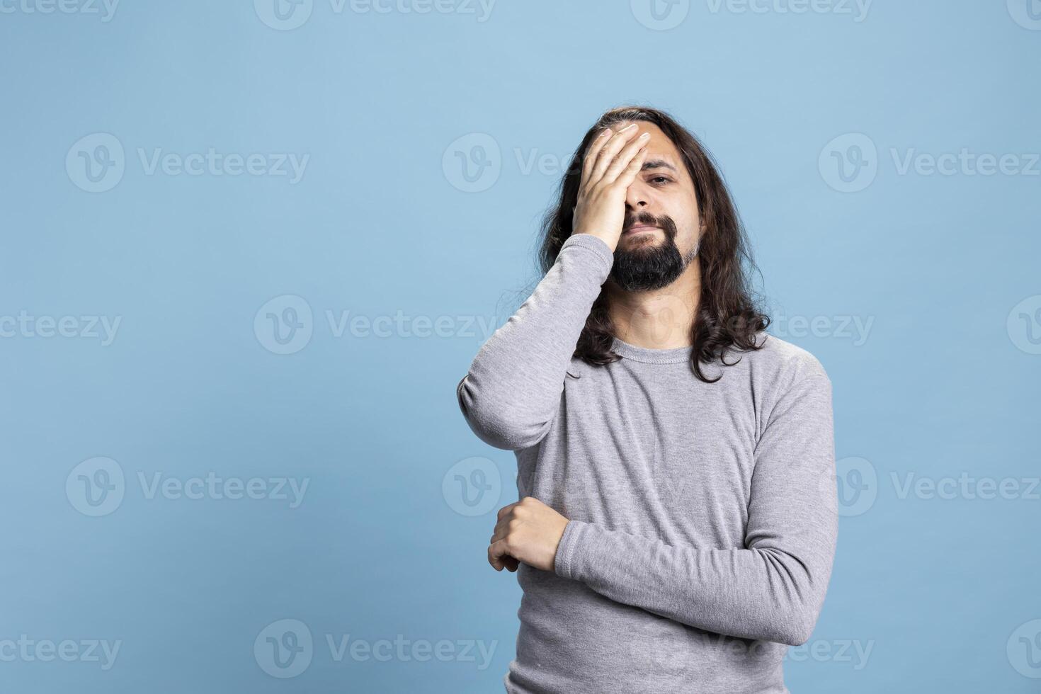 Young adult being stressed and unhappy about a misfortune in studio, dealing with sorrow and sadness against blue background. Discouraged depressed person feeling gloomy and hopeless. photo