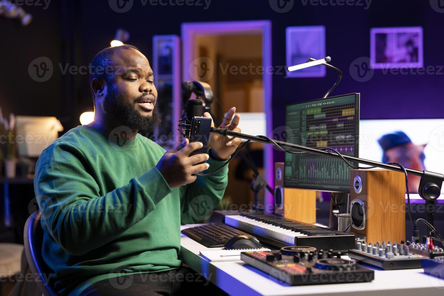 Talented young artist performing an acoustic version of his new song, reading the lyrics on his smartphone. Professional musician producing a new track, recording audio files on microphone. photo