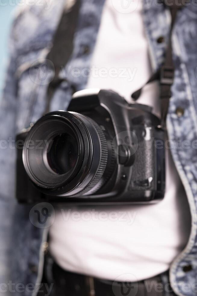Extreme closeup of a black camera. Selective focus on DSLR hanging from the neck of an individual in a denim jacket, with selective focus on the lens, highlighting intricate details. photo