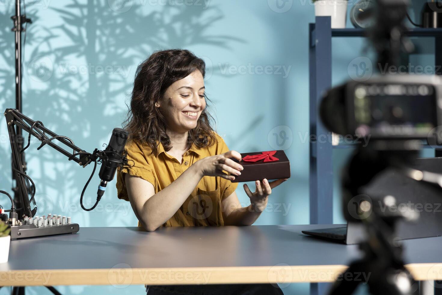 Joyful influencer holding giveaway for viewers, offering gift box, engaging with audience to drive engagement and increase participation. Cheerful woman organizing contest, explaining rules photo