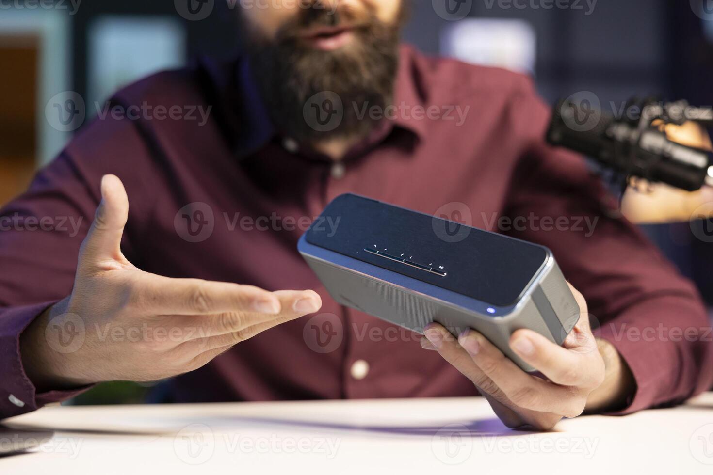 Man doing technology review of wireless portable speaker for internet vlogging channel. Close up shot of music playing device held by influencer showing it to his subscribers photo