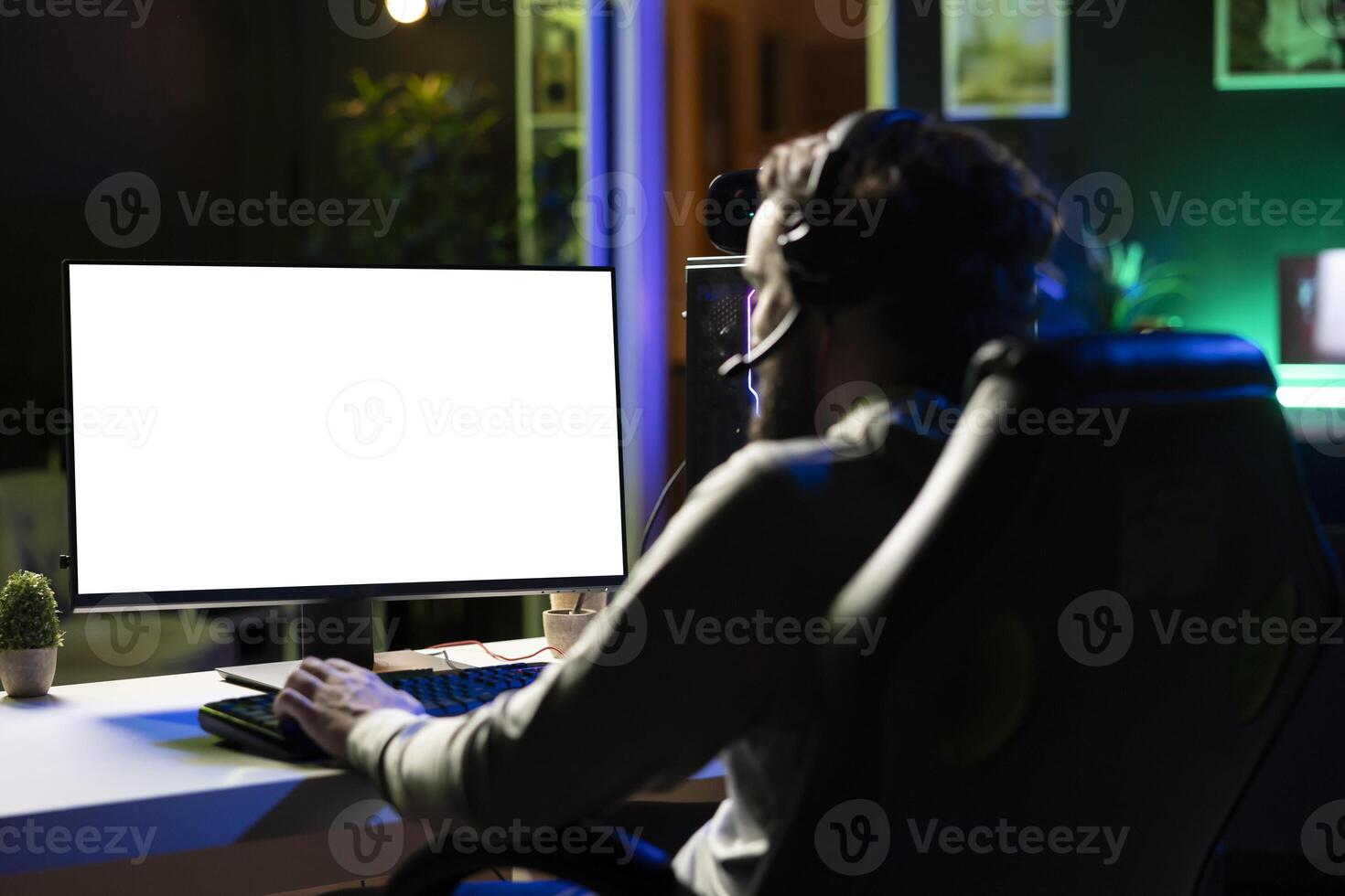 Man having fun by using isolated screen computer monitor to play singleplayer videogame. Professional gamer using mockup PC desktop to complete levels in game, talking with friends though headphones photo