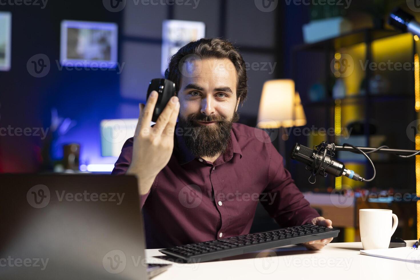 Cheerful tech expert filming review for online channel in apartment studio, analyzing office mouse for audience. Happy content creator recommending computer peripheral device photo