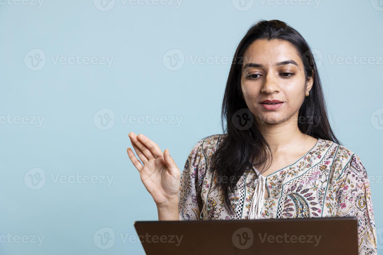 Happy indian girl waving hello on online conference in the studio, using device to stay in touch with her friends and family. Young relaxed woman on call connection, positive mood. photo