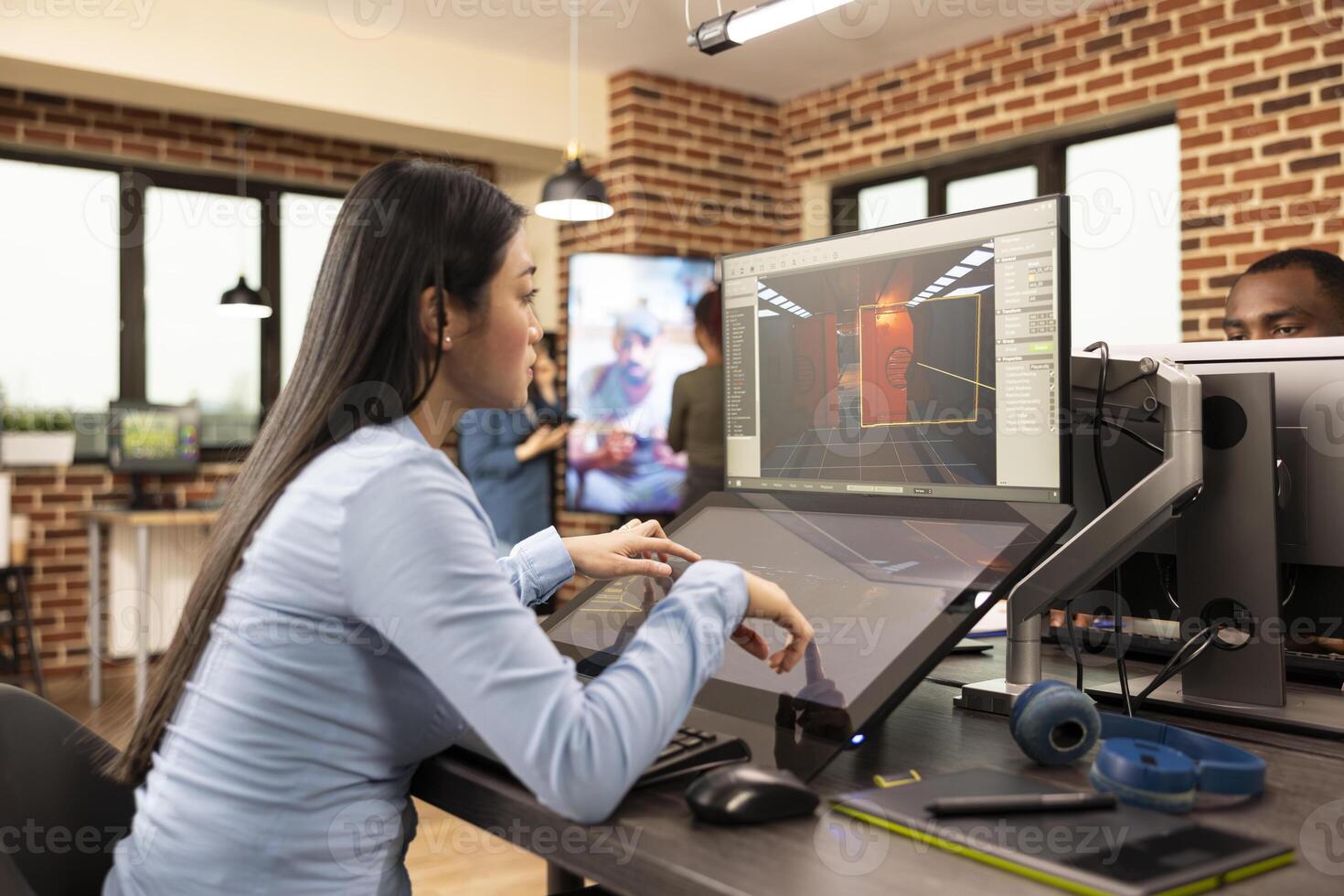 Asian game developer creates professional content in the production department, using touchscreen display. Skilled woman focuses on developing 3D game scenes and environments, utilizing multi screens. photo