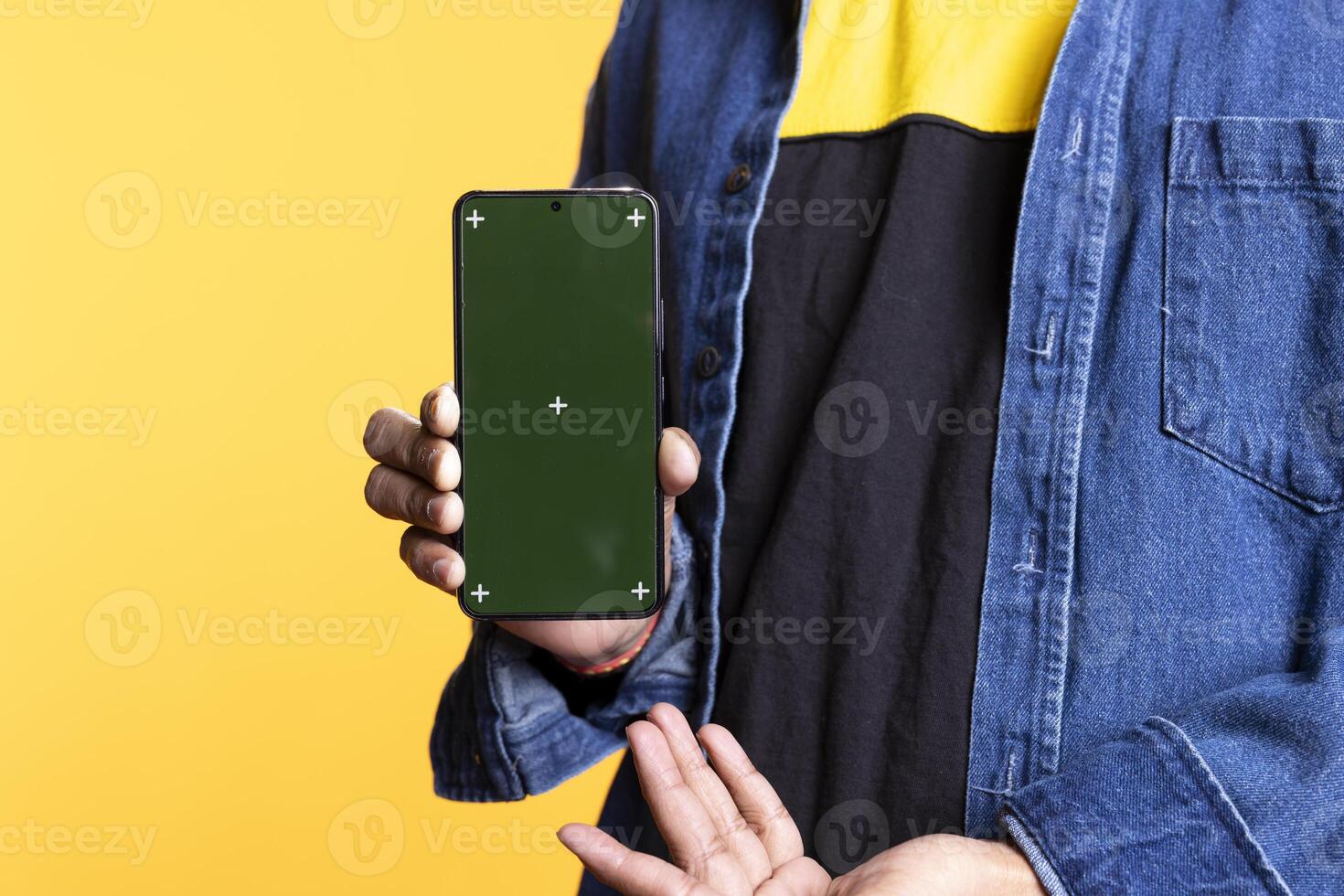 Confident casual person pointing at the copy space screen on gadget, pointing at the display on the mobile device. Young indian guy gesturing against orange background in studio. photo