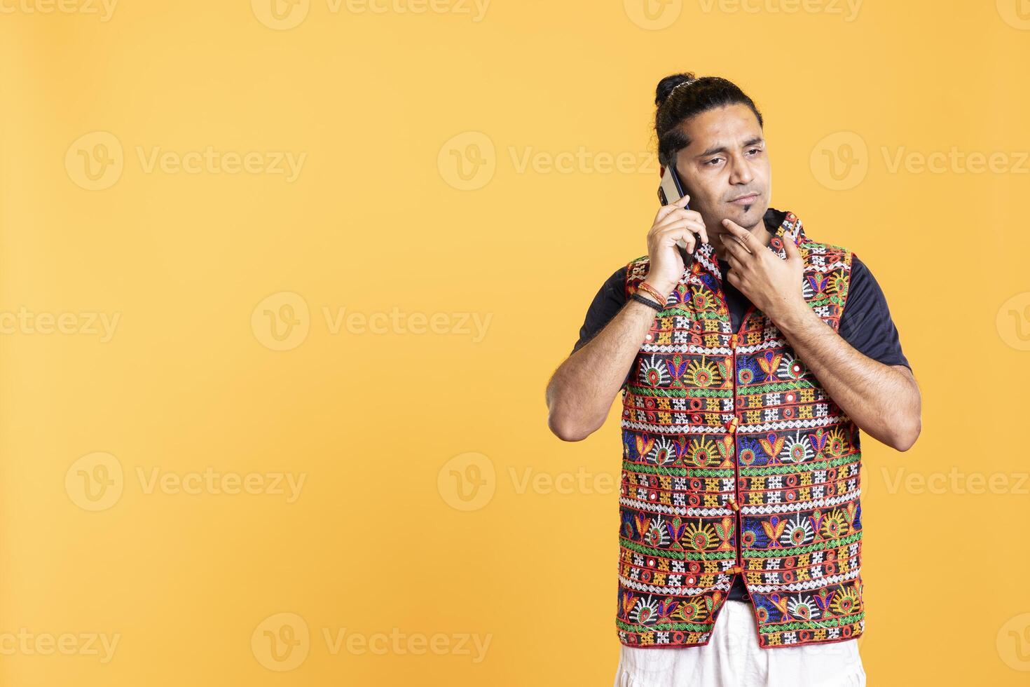 Overthinking man talking with friend on phone, doing stroking chin gesture during brainstorming. Pensive person discussing with mate during call, thinking, studio backdrop photo