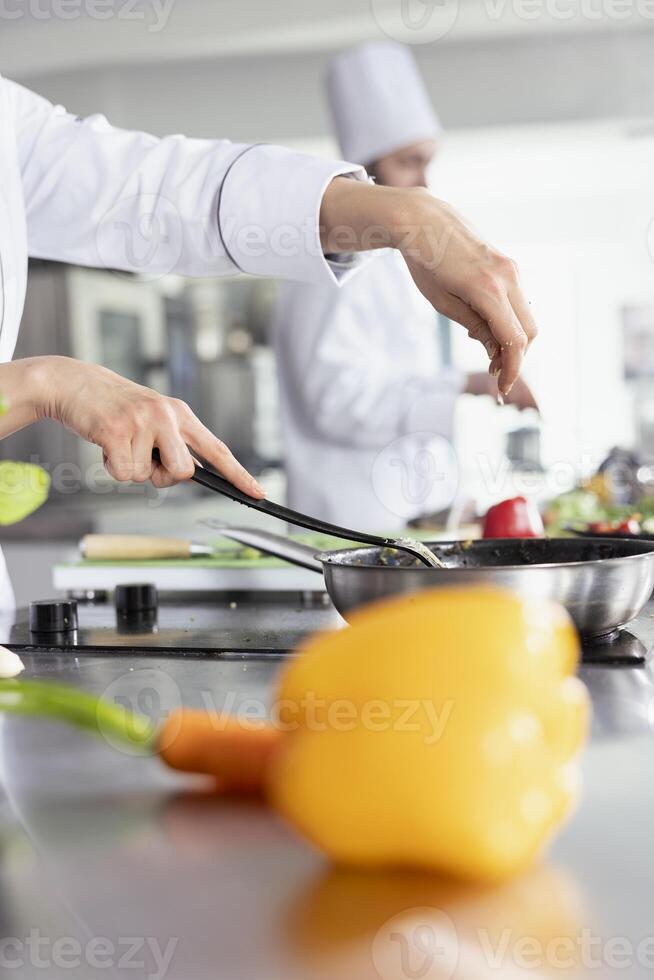 Female chef sprinkles fresh rosemary over a plated dish on the stove top, focusing on food plating and flavor. Preparing fresh ingredients, ensuring herbs in culinary workspace. Close up. photo