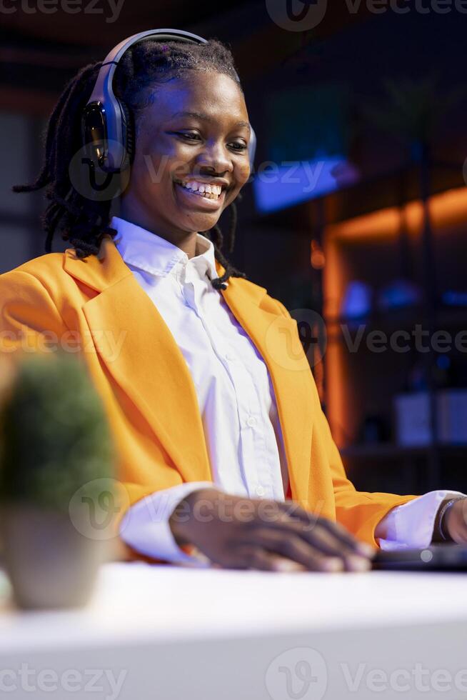 Joyous woman sitting at desk having fit of laughter watching funny comedy movie on laptop device. Upbeat person in apartment wearing headphones laughing hilarious joke in film scene on notebook photo