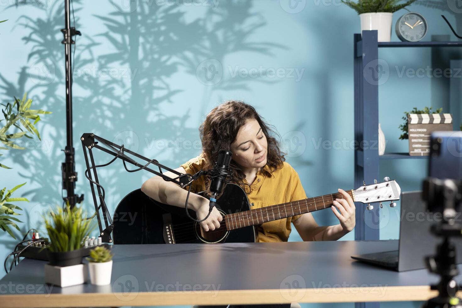 Talented artist playing music on guitar during livestream with viewers online, filming with smartphone. Woman using musical instrument, recording music with mobile phone, having fun photo