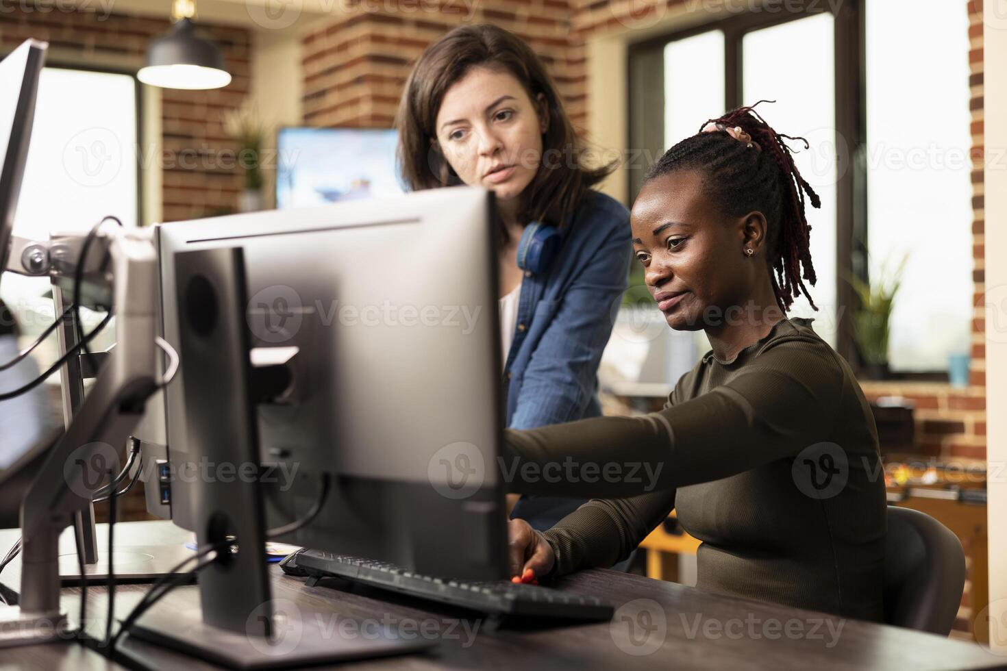 Production female team in creative agency brainstorms innovative ideas, using computer software to develop digital content. Black and caucasian women choosing new product designs on desktop pc. photo