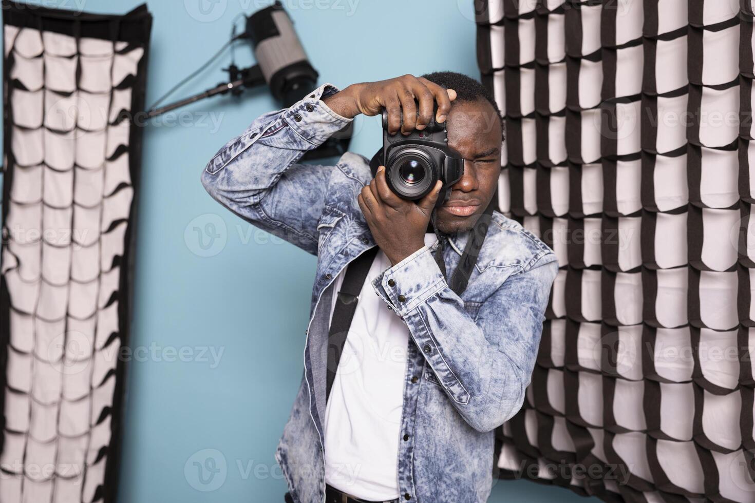 African American cameraman using his DSLR, highlighting his photography expertise. Young black photographer stands in studio, equipped with his camera gear and ready for photoshoot session with client. photo