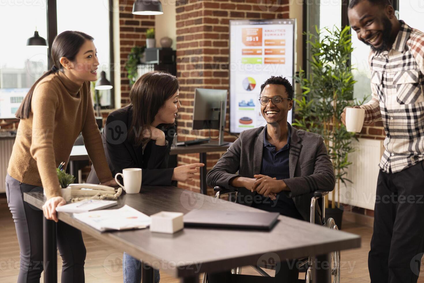 Businessman with a disability happily chatting with his diverse colleagues in a modern office. Excited employees from various backgrounds celebrating a company milestone together at startup company. photo