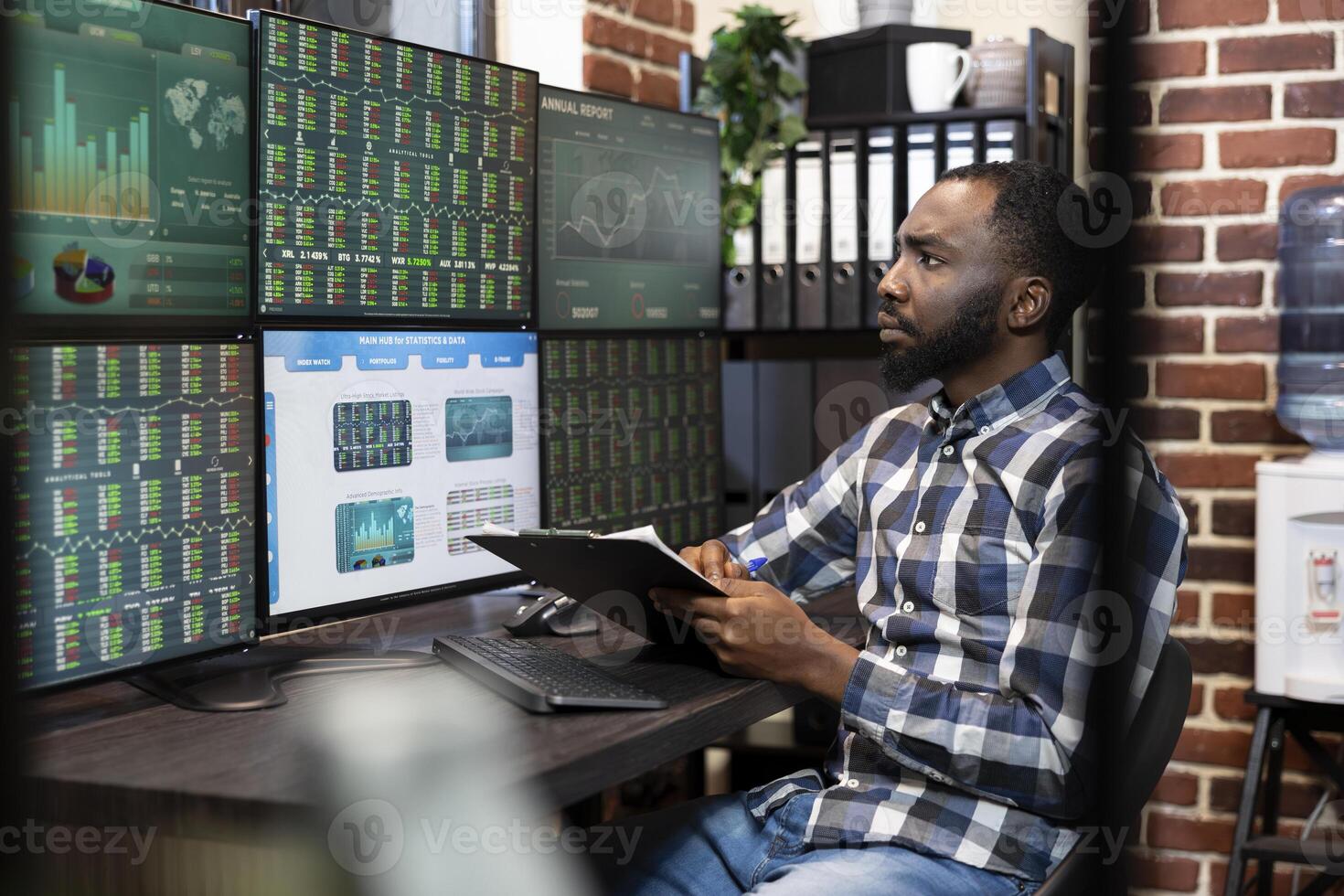 Male stock market trader with a clipboard in hand, analyzing real time data on a multi monitor setup in a dimly lit office. The scene reflects financial analysis and late night investment decisions. photo