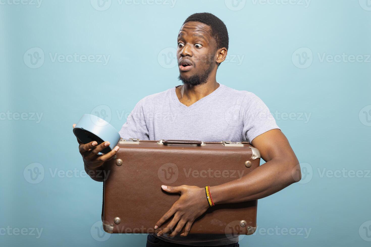 Shocked man with a luggage realizing how much time has passed, feeling anxious about being late for departure. Black male traveler carrying suitcase and checking his clock with surprised expression. photo