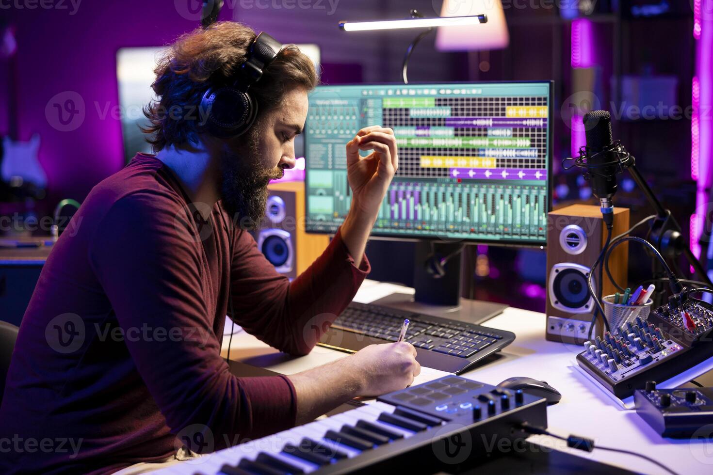 Composer songwriter taking notes to create a new song in his home studio, writing down lyrics and musical notes before recording his tune on mixing console and microphone, music industry. photo