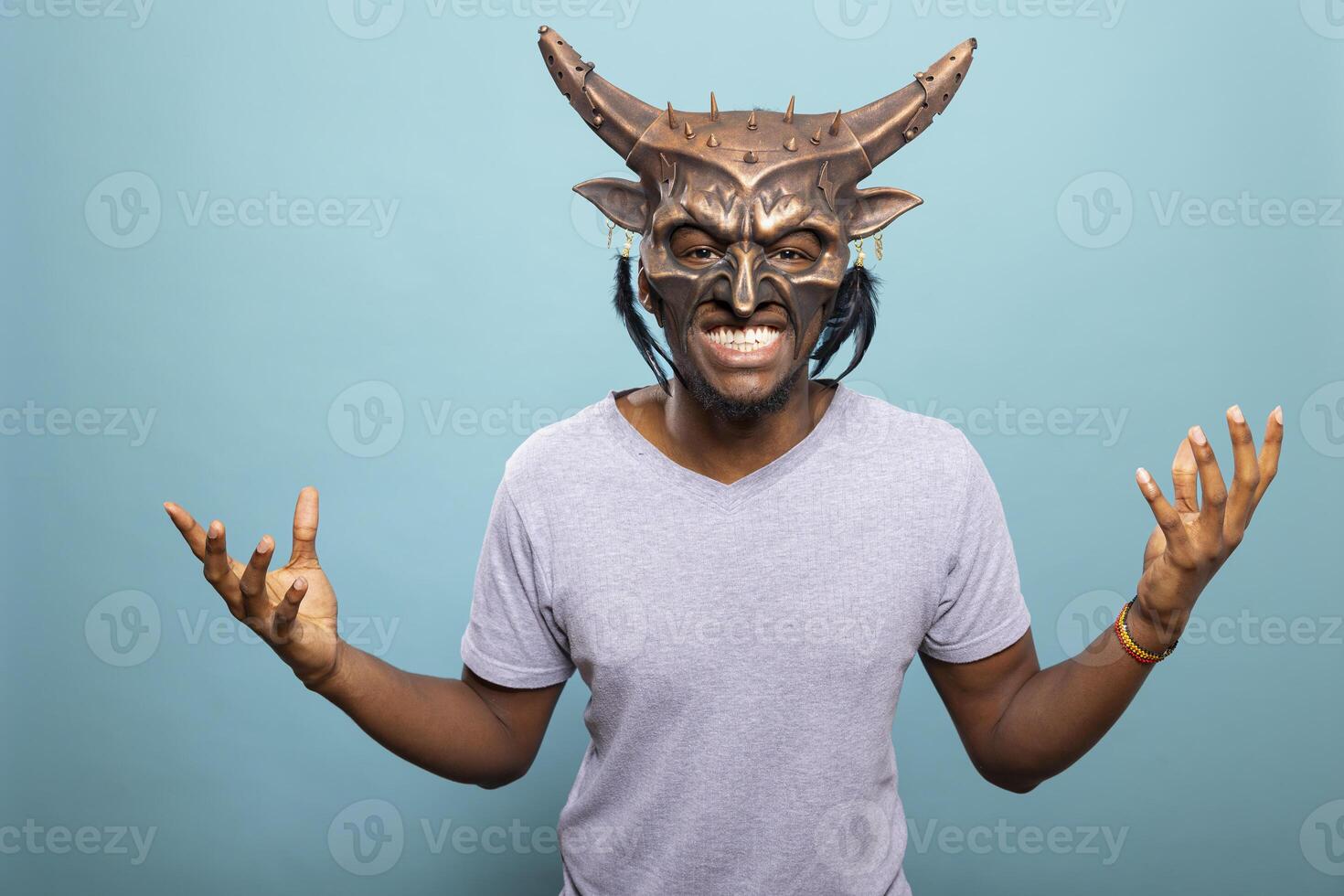 Portrait of male model wearing creepy monster costume mask, posing with hands raised for dramatic effect. Closeup of man wearing creature mask, embodying spooky character with eerie facial movements. photo