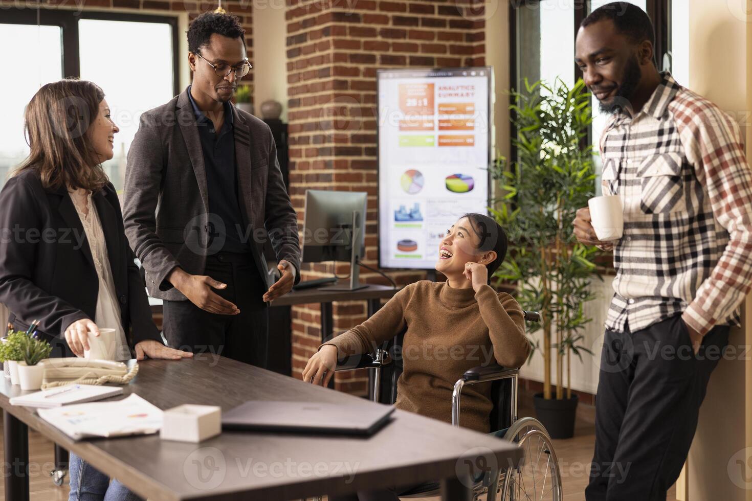 Multiracial professionals in a creative startup office taking a moment to unwind, chatting and laughing together during a break. African american man with glasses, sharing a story to his team. photo
