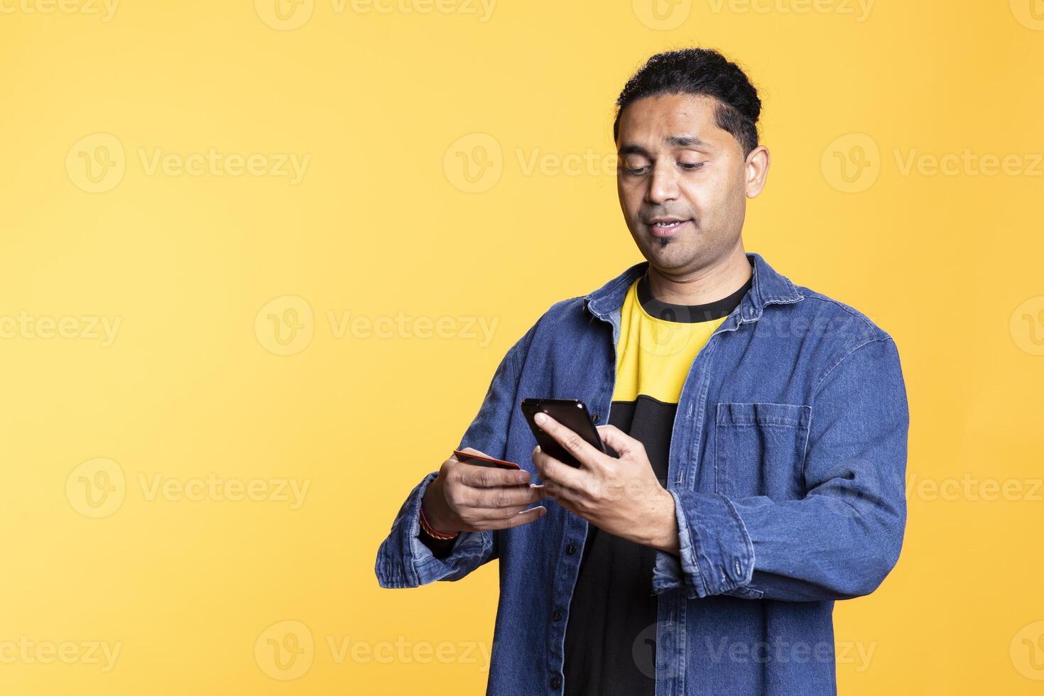 Indian man adding payment method on online website with his card, delighted to take advantage of promotions in the studio. Young person thrilled to do internet shopping, typing credit card data. photo