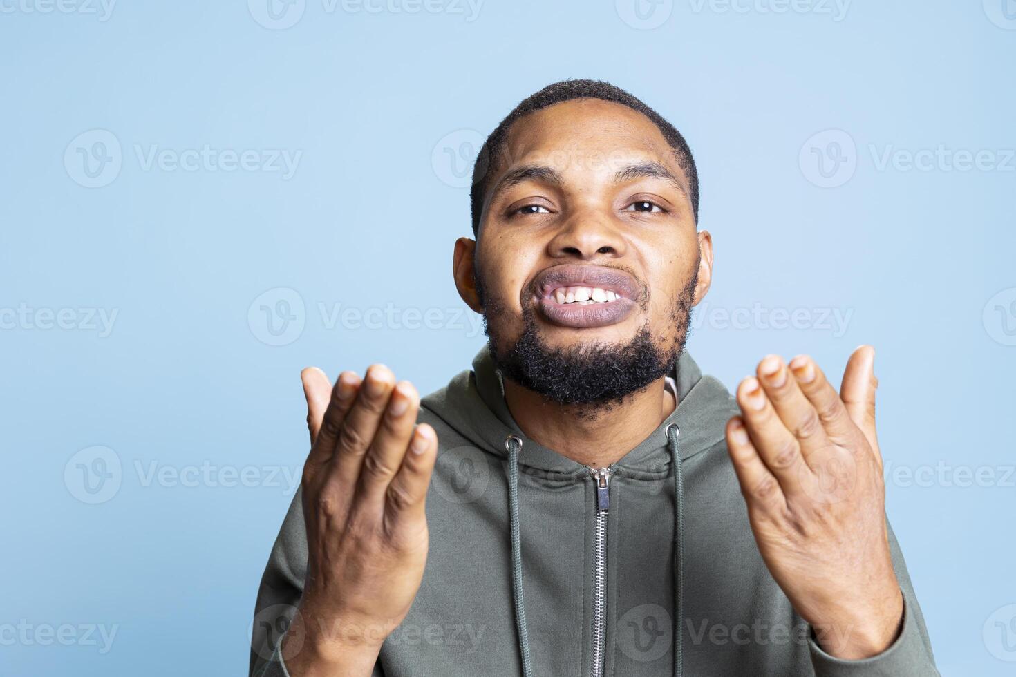Cute young person sending air kisses to the audience and showing his gratitude, acting sweet with this gesture against blue background. African american guy being lively and positive in studio. photo