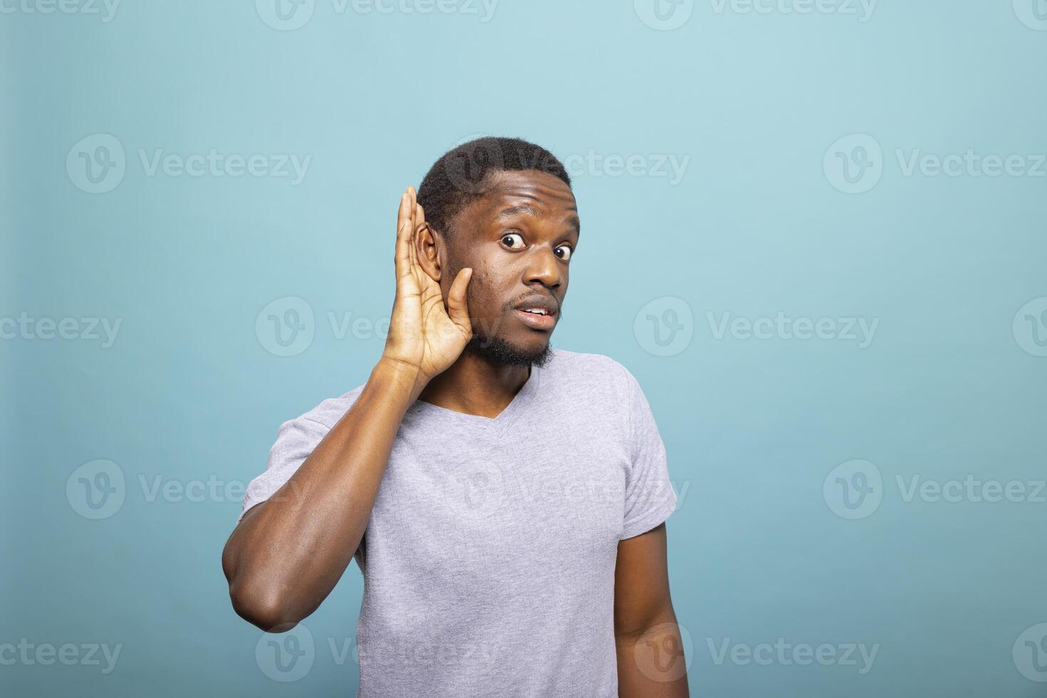 African American man cupping his ear to hear better, expressing curiosity and interest. Portrait of a black male individual listening closely, eavesdropping on a conversation. photo