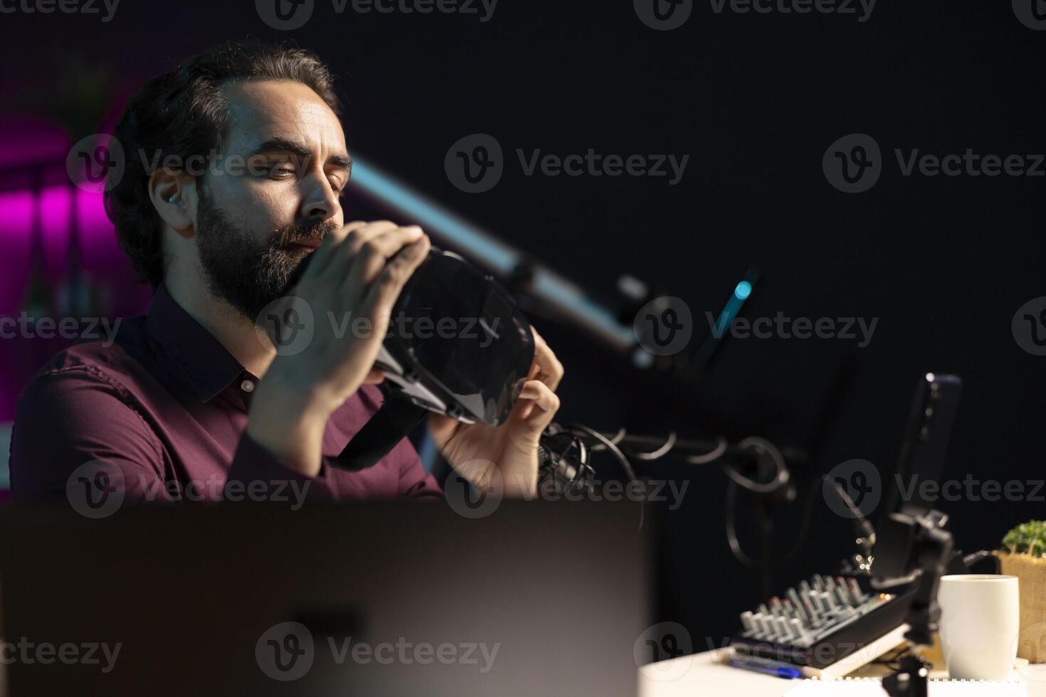 Man presenting VR goggles to audience, filming with smartphone on tripod. Content creator assessing virtual reality headset product before recommending it to fans, filming with mobile phone photo