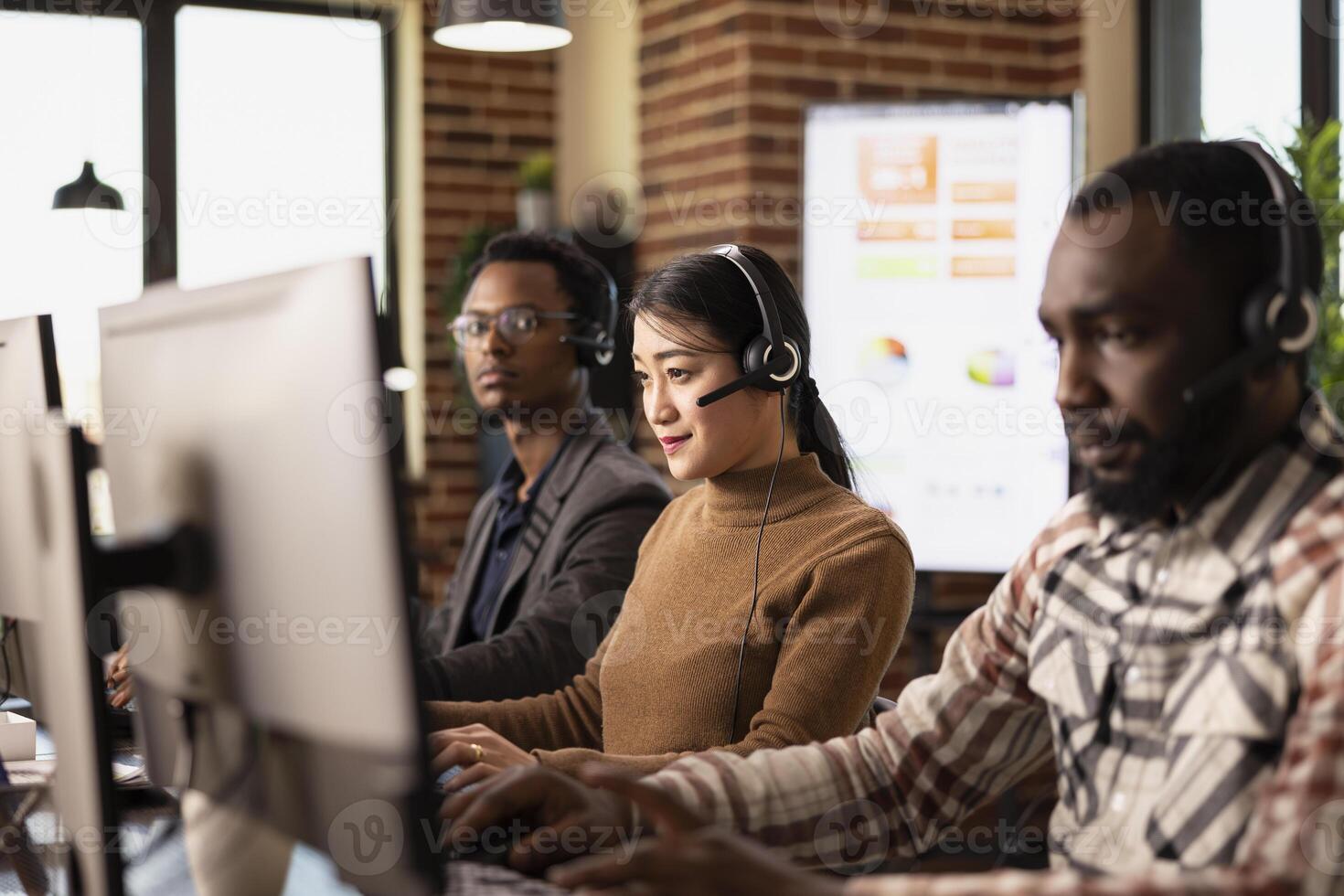 Selective focus of female employee working together with african american colleagues, providing remote client support. Asian woman analyzing customer feedback on a desktop computer. photo