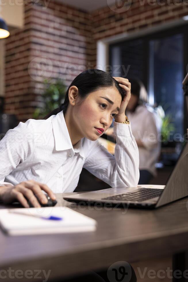 Stress and fatigue are evident as a businesswoman works late into the night in a modern office, managing her workload and responsibilities under pressure. Career burnout and stress management. photo