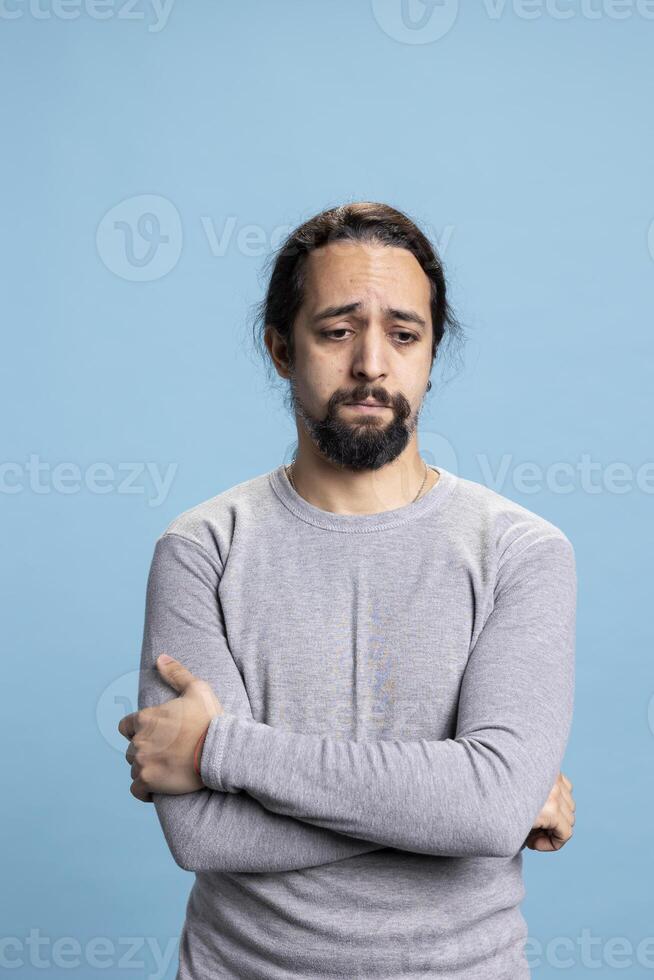 Depressed anxious adult dealing with low self esteem against blue background, whining and being in an emotional crisis. Melancholic person with distress and desolation, disappointed guy. photo