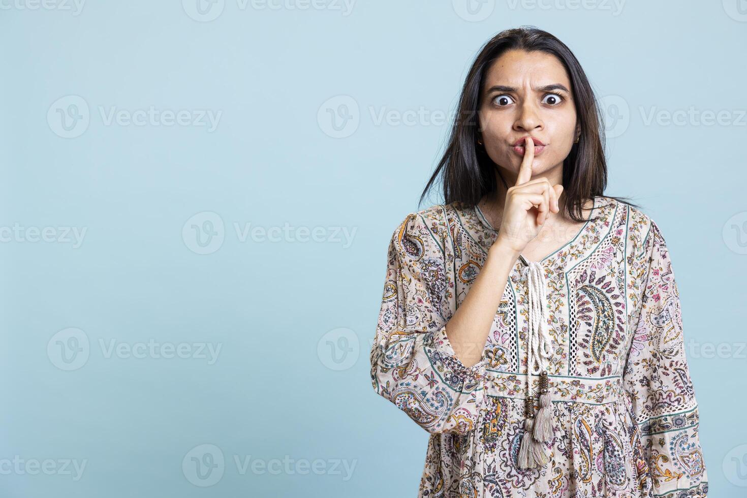 Private person doing mute silence hand gesture in front of camera, demanding secrecy and being irritated by noise. Indian person complaining, placing finger on lips and doing quiet warning sign. photo