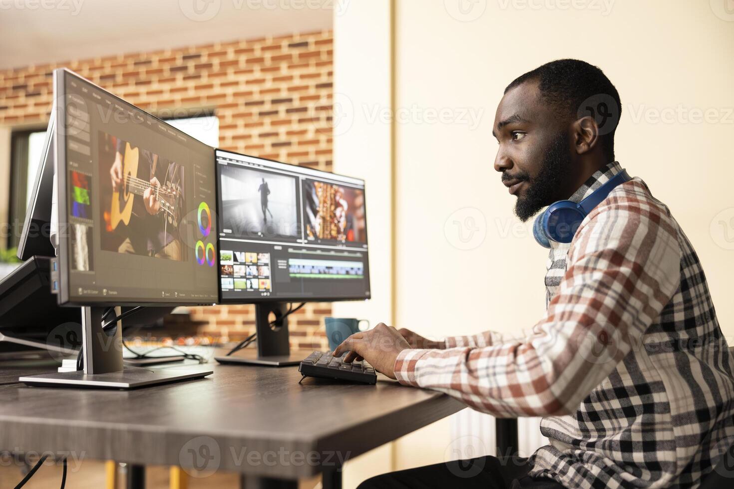 Black male editor with headphones, enhancing quality of digital footage on computer screens. African american production specialist using multi monitor setup to refine movie frames. photo