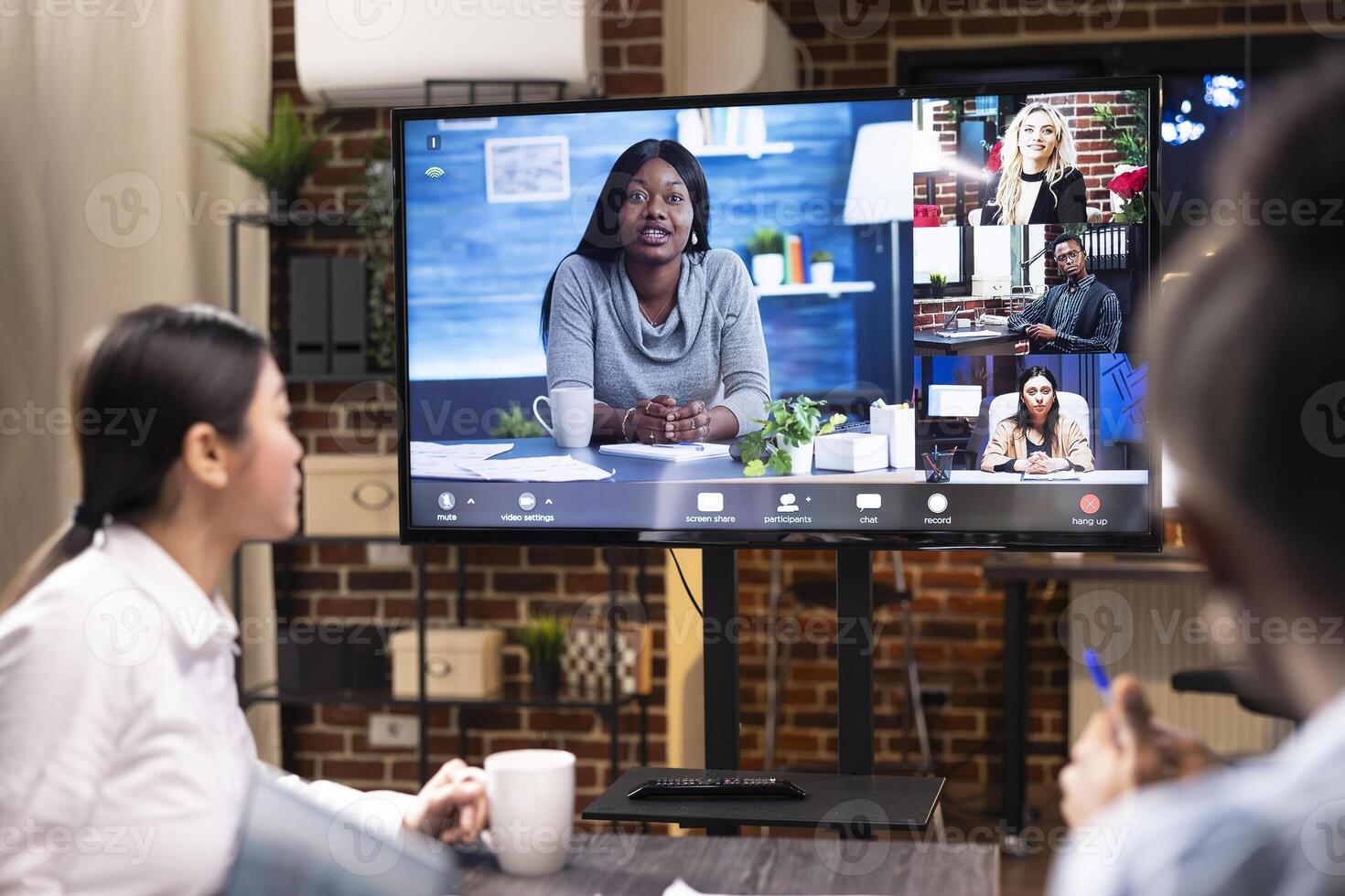 Entrepreneurs in startup office participating in videoconference to discuss project planning. Multiethnic coworkers use digital monitor to collaborate on business goals and marketing tactics remotely. photo