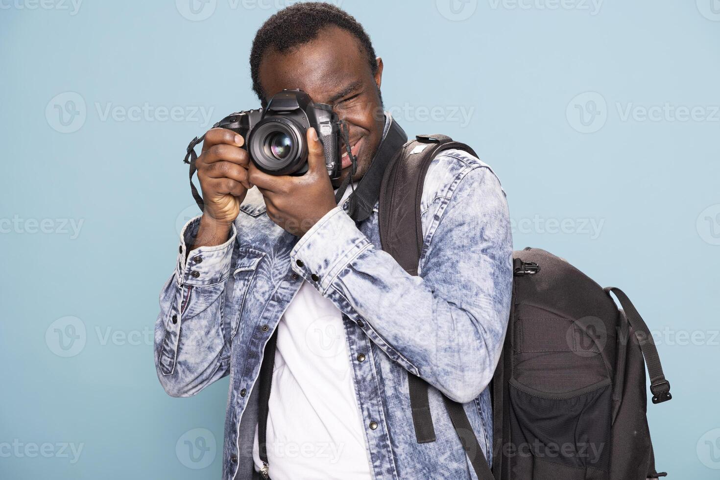 Young black man lifts his DSLR camera, focusing on his next shot with precision. His relaxed yet concentrated stance highlights his role as a modern content creator and visual storyteller. photo