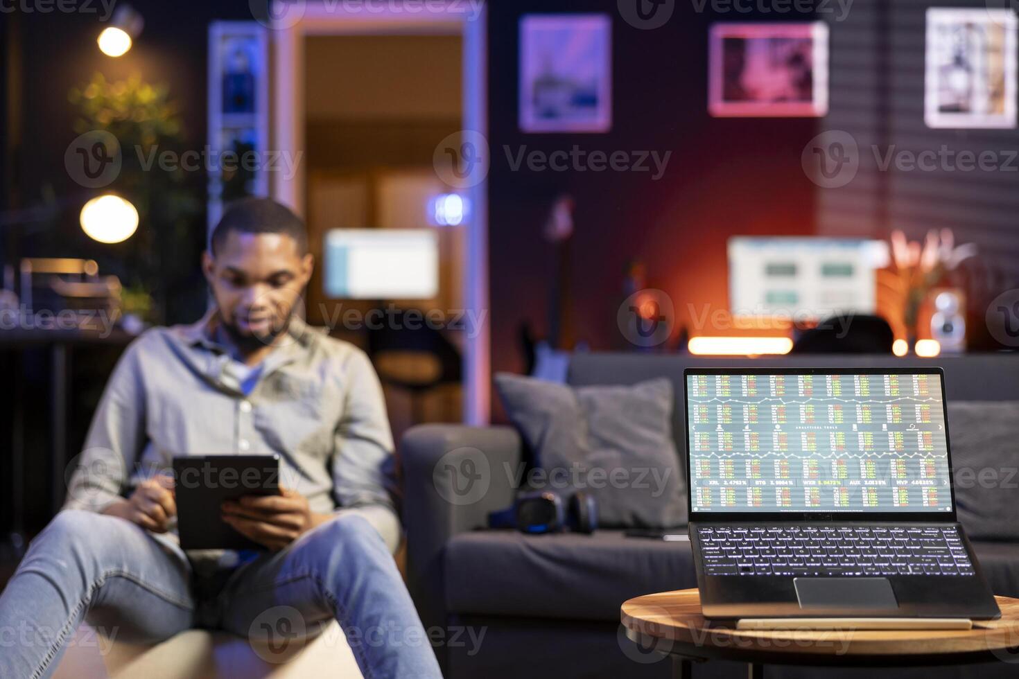 Black man day trading from home on laptop following stock market charts and financial graphs. Remote work setup shows an investor tracking prices, trends and data for online investment decisions. photo