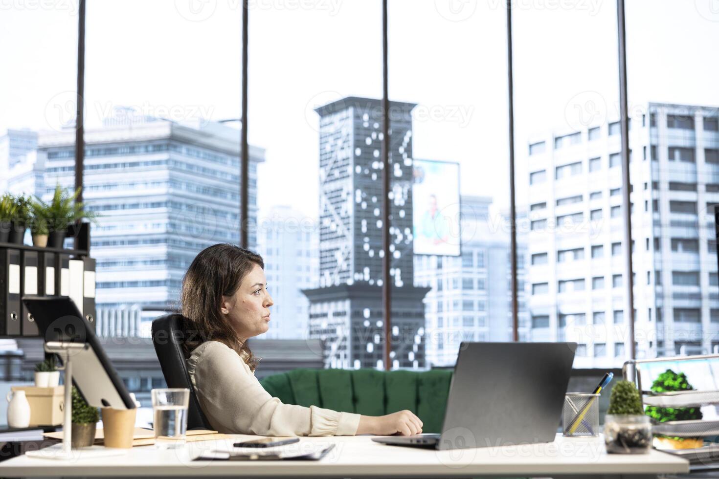 Powerful influential woman director taking a break and relaxing in her office, admiring the urban city view from her window. Female chief executive officer resting in her high end workspace. photo