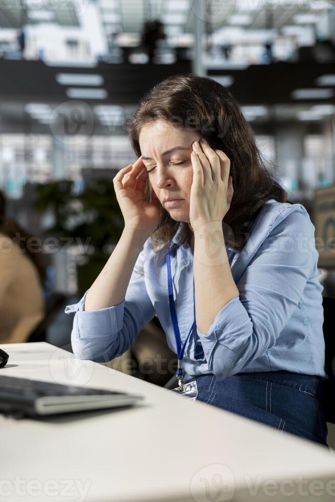 Exhausted overworked woman being unwell with a migraine at the office, trying to overcome stress and pressure but feeling unhappy. Worried tired employee with a serious headache. photo