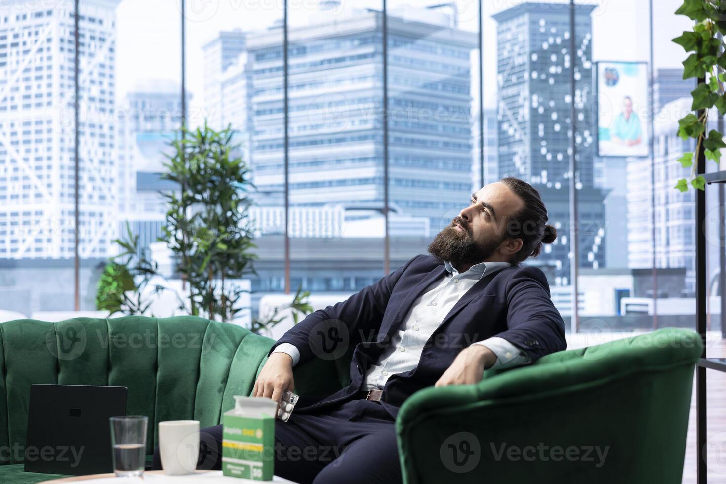 Overworked fatigued boss swallowing an aspirin to ease his headache, taking painkillers to help with his burnout and workload. Young CEO being anxious and overwhelmed in the office. photo