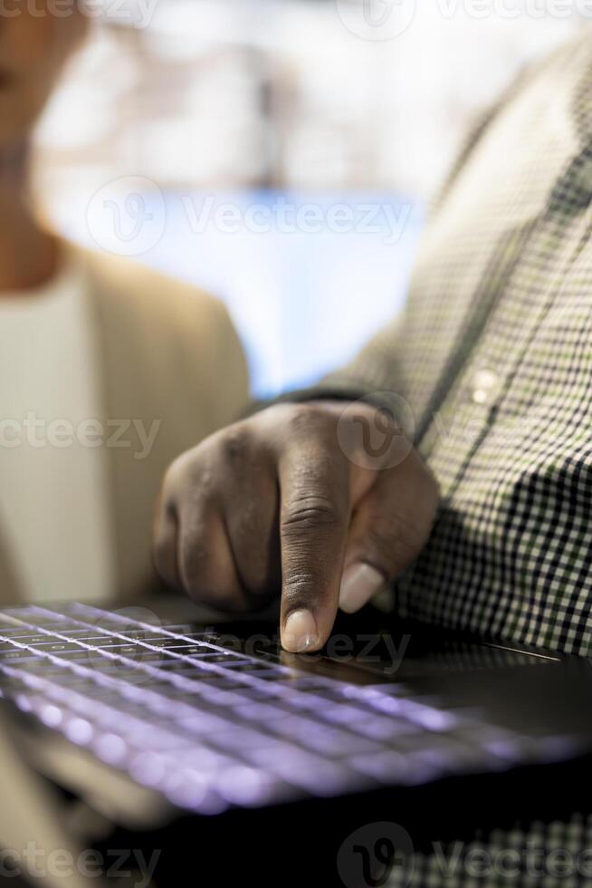 African american man next to colleagues in office coordinating company administrative operation, writing documents on notebook. Close up of employee typing on laptop keyboard, inputting data metrics photo